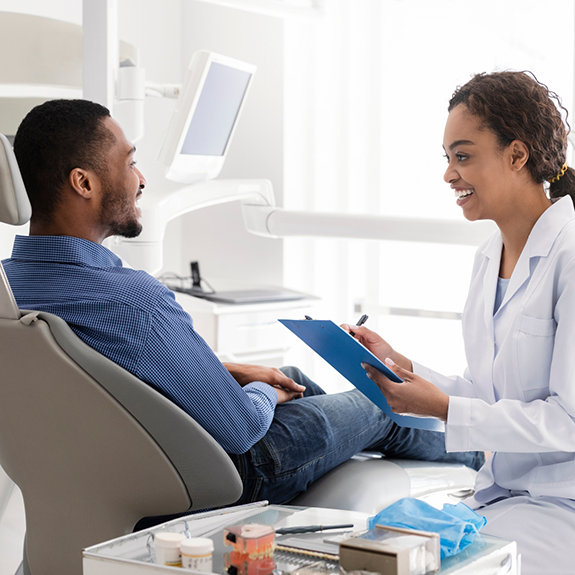 Dentist holding clipboard and talking to patient