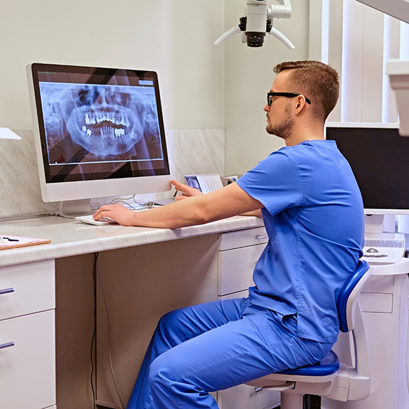 Man in glasses looking at dental X-rays on computer