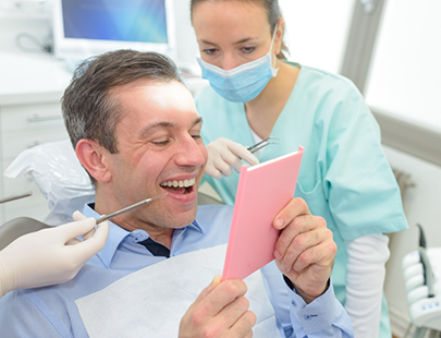 Male dental patient checking smile in handheld mirror