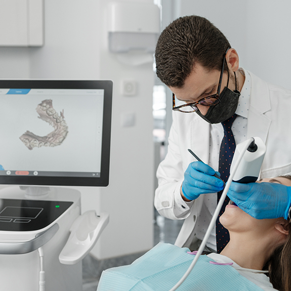 Dentist with glasses taking digital impressions of patient's mouth