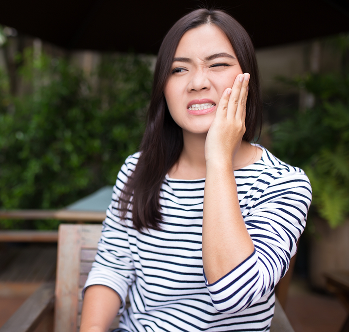 Woman in striped shirt rubbing jaw in pain