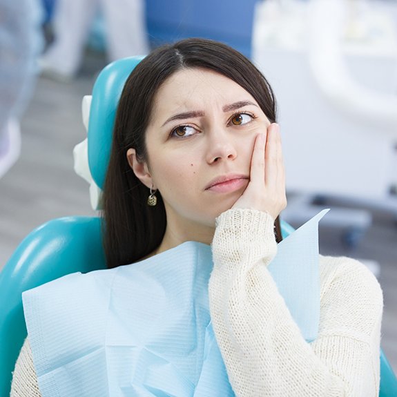 Woman in sweater sitting in dental chair looking concerned