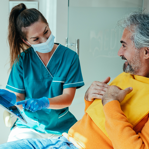 Dentist with mask talking to patient in yellow shirt