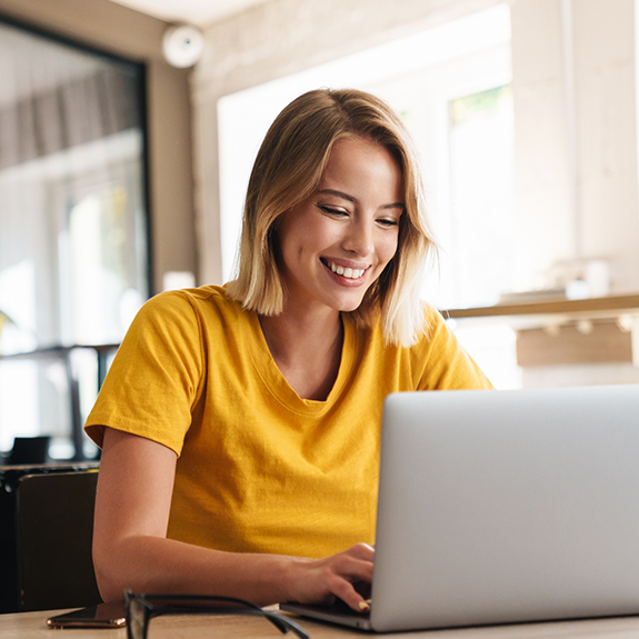 Woman in yellow shirt typing on laptop