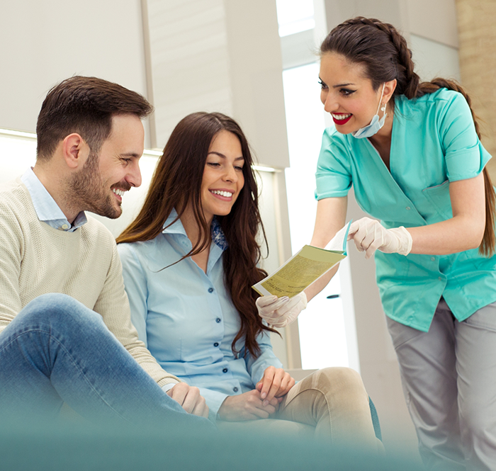 Dental team member showing man and woman a piece of paper