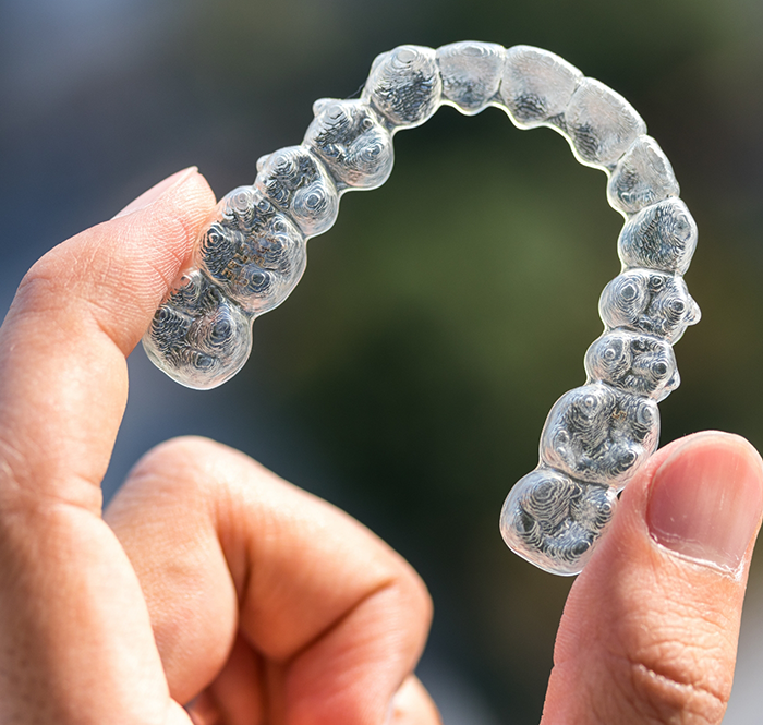 Close up of hand holding an Invisalign clear aligner in Flower Mound