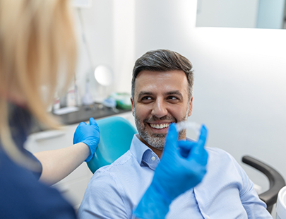 Male patient looking at clear aligner held by female dentist