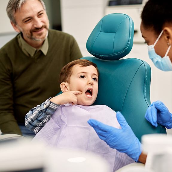 Boy in dental chair holding mouth open for dentist