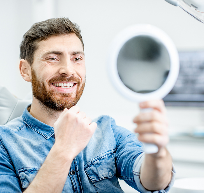 Man with beard looking at handheld mirror and smiling