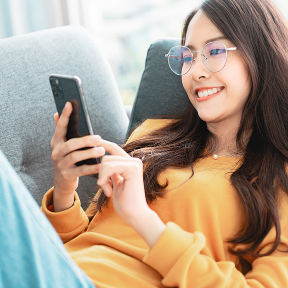 Woman with glasses lying on couch and looking at phone